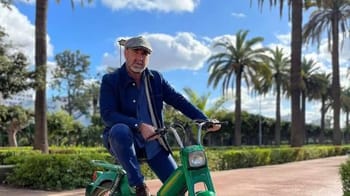 Eric Cantona en promenade dans un parc algérien avec palmier.