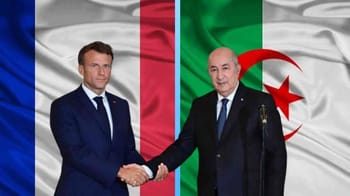 Deux hommes se serrent la main devant un drapeau algérien et français.