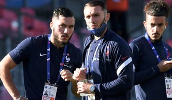 Trois joueurs de football en préparation, portant des badges et des tenues sportives.