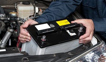 Personne vérifiant la batterie d'une voiture dans un garage.