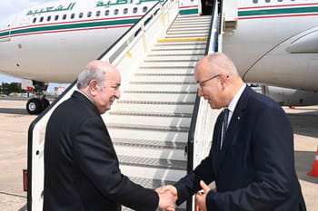 Tebboune et un officiel se serrent la main à l'aéroport.