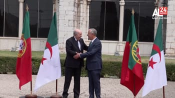 Deux hommes en costume se serrent la main devant des drapeaux portugais et algériens.