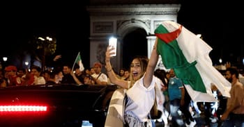 Femme algérienne souriante avec drapeau algérien lors d'une célébration nocturne.