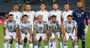 Groupe de joueurs de football algériens en tenue blanche sur le terrain.
