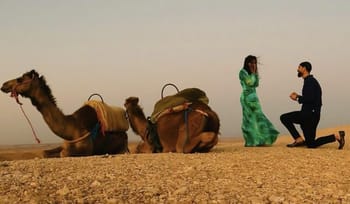 Homme faisant une demande en mariage à une femme dans le désert avec des chameaux.