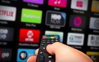 Main tenant un contrôleur TV face à un écran d'applications de streaming.