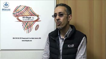 Homme en studio radio Ifrikya FM avec logo en arrière-plan.