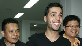 Jeune homme souriant avec deux autres personnes dans un environnement intérieur.