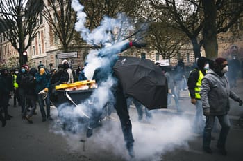 Manifestation avec gaz lacrymogène et protestataires masqués dans la rue.