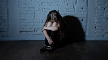 Jeune fille assise par terre, visage caché, dans une ambiance sombre et isolée.