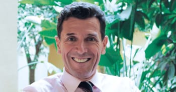 Homme souriant avec un décor de plantes luxuriantes.