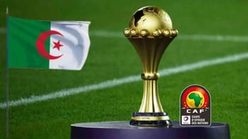 Trophée de la CAN avec drapeau algérien en arrière-plan.