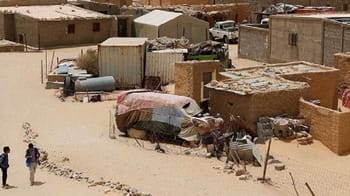 Village saharien avec habitations en terre et véhicules dans le désert.