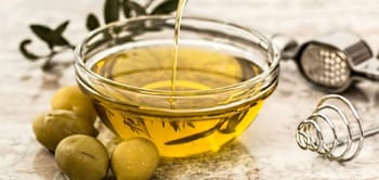 Huile d'olive algérienne dans un bol en verre avec olives vertes.