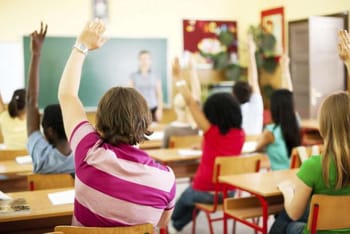 Enfants en classe levant la main lors d'une activité scolaire.