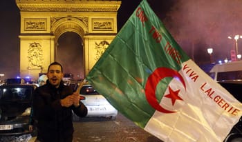 Homme tenant un drapeau algérien devant l'Arc de Triomphe à Paris.