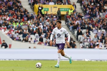 Farès Chaïbi joue au football sur le terrain avec un public en arrière-plan.