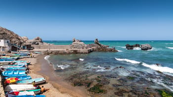 Plage en Algérie avec bateaux et rochers, vue sur la mer Méditerranée.