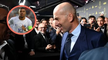 Zinédine Zidane souriant lors d'un événement avec Kylian Mbappé en arrière-plan.