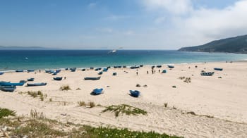 Plage de sable propre avec des bateaux abandonnés et une mer claire.