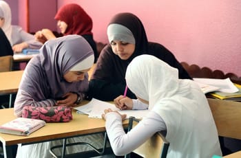 Jeunes femmes musulmanes en classe, portant des hijabs, concentrées sur leurs devoirs.