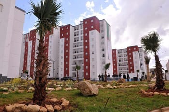 Immeuble résidentiel moderne avec jardins et palmiers en avant-plan.