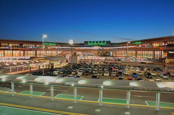 Parking d'aéroport de Nador avec voitures et terminal illuminé.