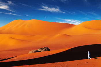 Paysage désertique avec dunes orange et ciel bleu clair.