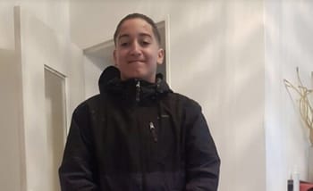 Jeune garçon souriant portant une veste noire dans une pièce intérieure.