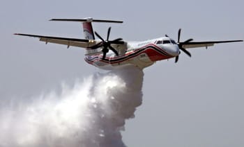 Avion bombardier d'eau déployant de l'eau contre un feu de forêt.