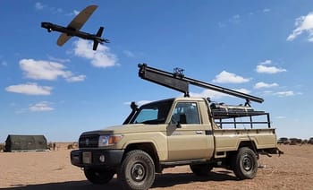 Véhicule militaire dans le désert avec drone en vol dans le ciel bleu.