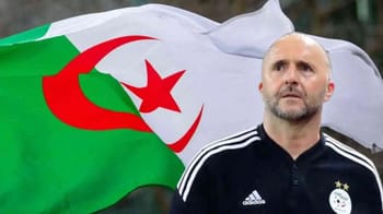 Belmadi devant drapeau algérien lors d'une rencontre sportive.