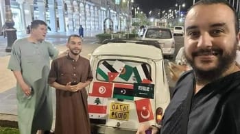 Homme souriant devant une Renault 4 décorée pour le pèlerinage à la Mecque.