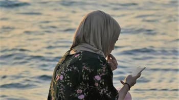Femme en hijab regardant son téléphone au bord de l'eau.