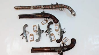 Collection de pistolets et fusils anciens en vitrine.