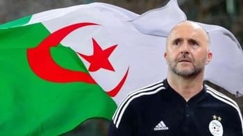 Homme avec barbe devant drapeau algérien en fond.