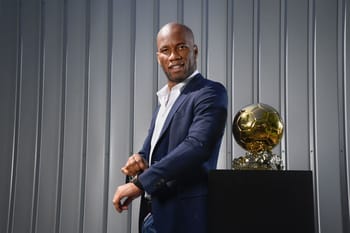 Didier Drogba en costume avec un ballon dor en arrière-plan.