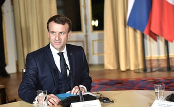 Emmanuel Macron assis à une table lors d'une conférence officielle.