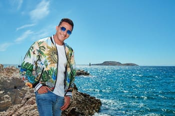 Homme souriant en tenue décontractée près de la mer ensoleillée.