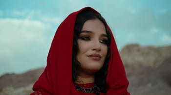 Numidia Lezoul portant un voile rouge dans un paysage désertique.