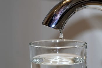 Goutte d'eau tombant dans un verre sous un robinet.