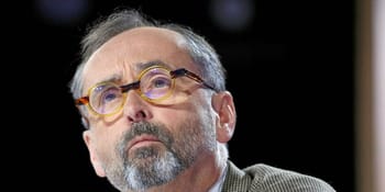 Homme avec lunettes, barbe grise, expression sérieuse.