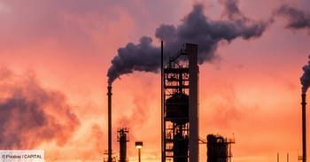 Usine pétrolière avec fumée s'élevant au coucher du soleil.