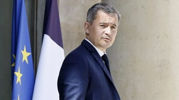 Gérald Darmanin en costume sombre, fond de drapeaux français et européens.