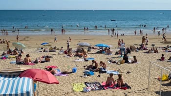 Plage animée en Algérie avec des touristes et des parasols colorés.