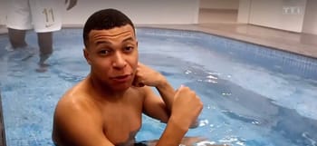 Kylian Mbappé dans une piscine, regardant l'objectif, ambiance détendue.