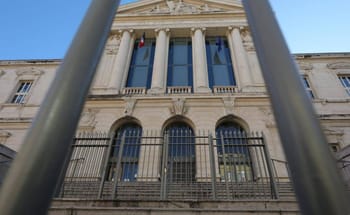 Vue du palais de justice de Nice à travers une grille en fer forgé.