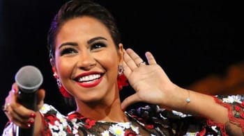 Chanteuse souriante lors d'un concert, portant une robe colorée et des boucles d'oreilles.