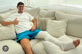 Jeune homme souriant avec jambe en plâtre sur canapé blanc.