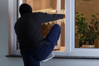Cambrioleur masqué essayant d'ouvrir une fenêtre à l'aide d'un outil.